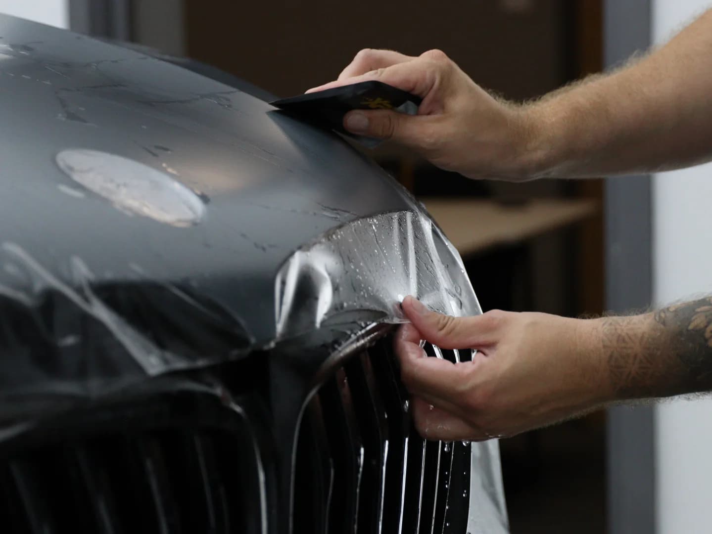 A technician working paint protection film into a car's panel gaps