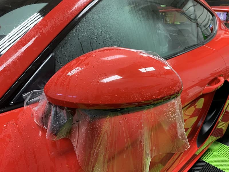 Paint protection film going onto a red Porsche's wing mirror